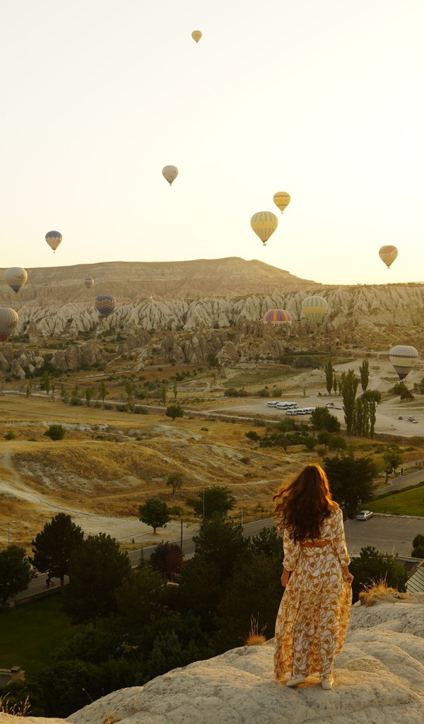 Девушка стоит на краю скалы на фоне неба с воздушными шарами