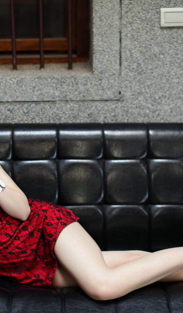 Молодая девушка азиатка лежит на черном кожаном диване