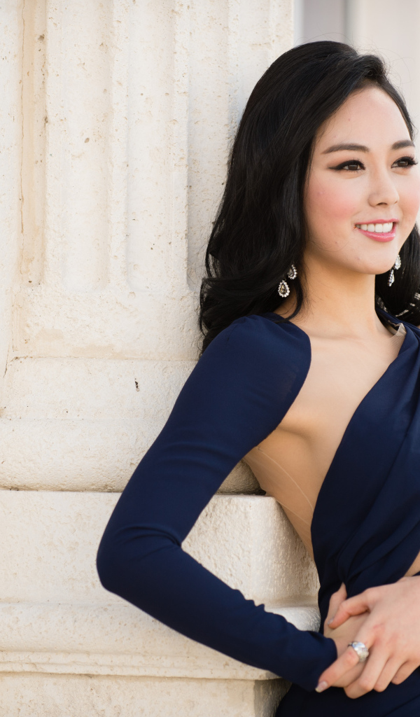 Молодая девушка в платье стоит у стены 