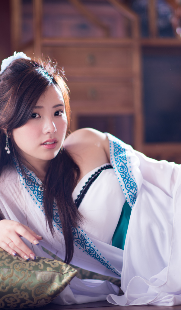 Девушка азиатка в красивом платье лежит на кровати 