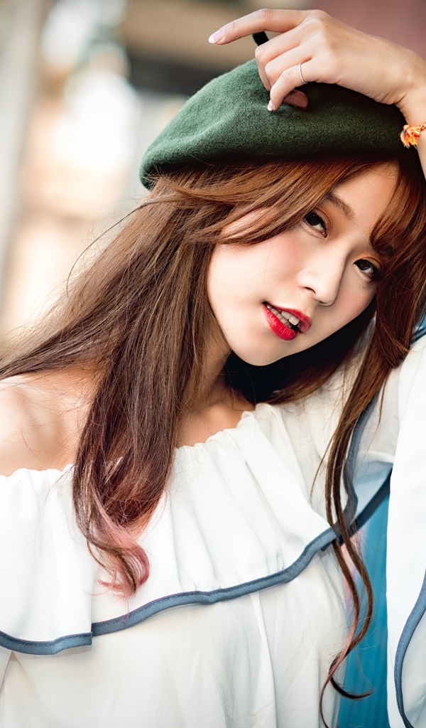 Девушка азиатка в берете стоит у стены 