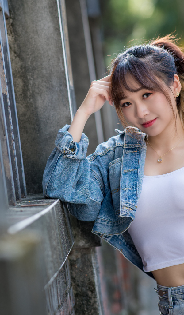 Девушка азиатка в джинсовой куртке у забора 