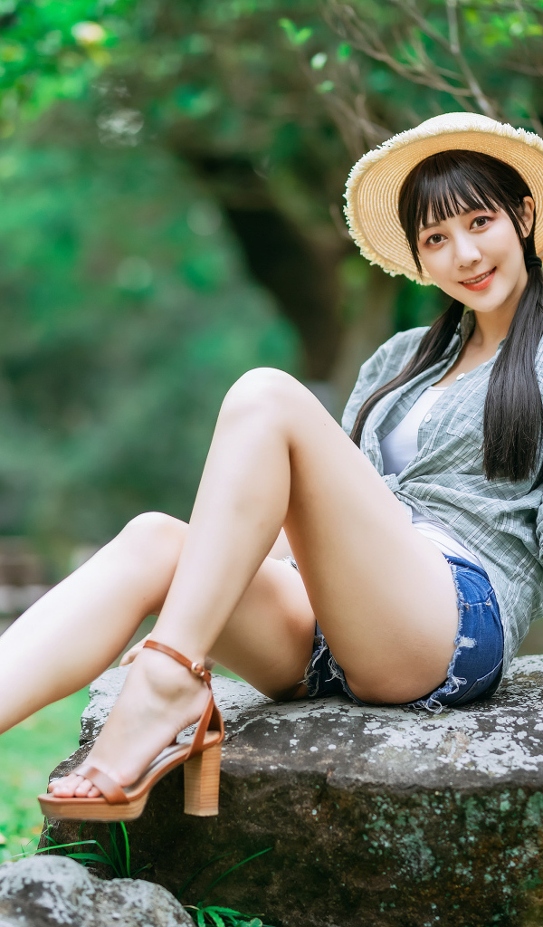 Девушка азиатка в шляпе сидит на камне