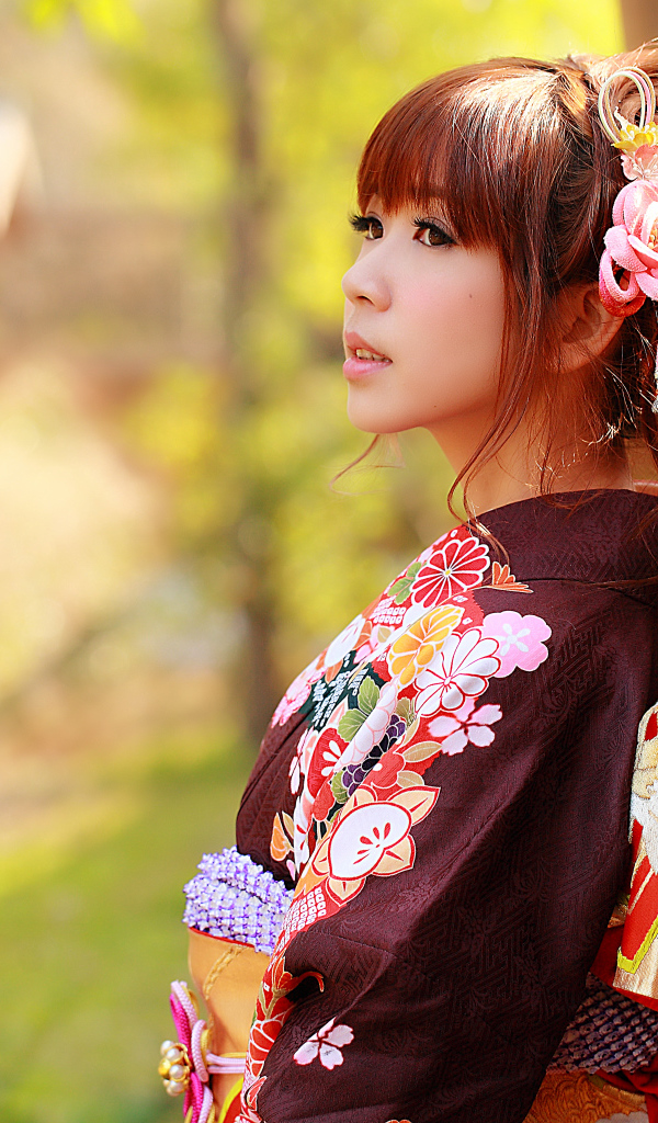 Девушка азиатка в кимоно стоит у забора 