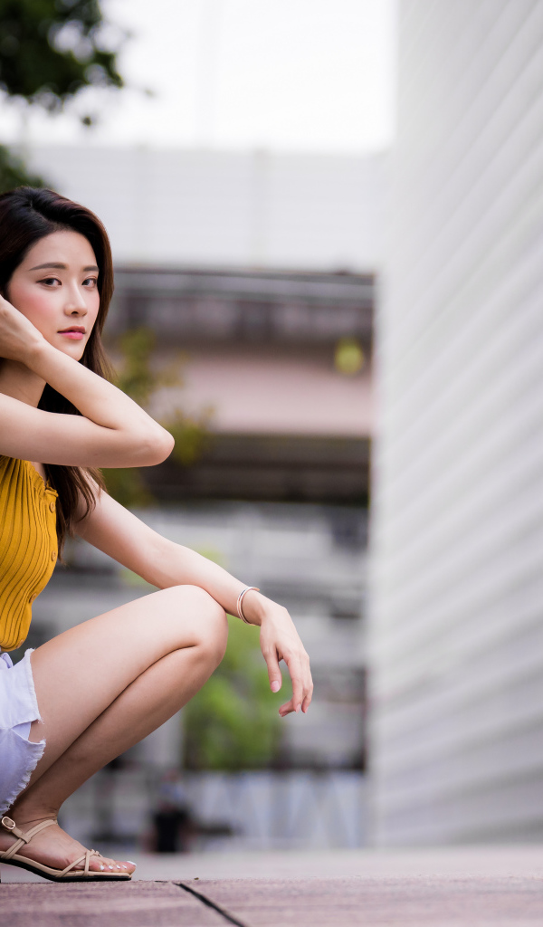 Девушка азиатка сидит на корточках у стены