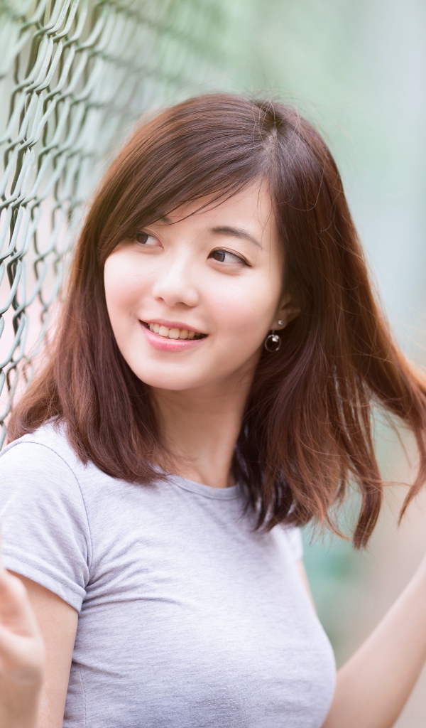 Девушка азиатка с милой улыбкой стоит у сетки 