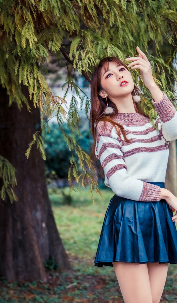 Красивая девушка азиатка стоит у дерева в парке