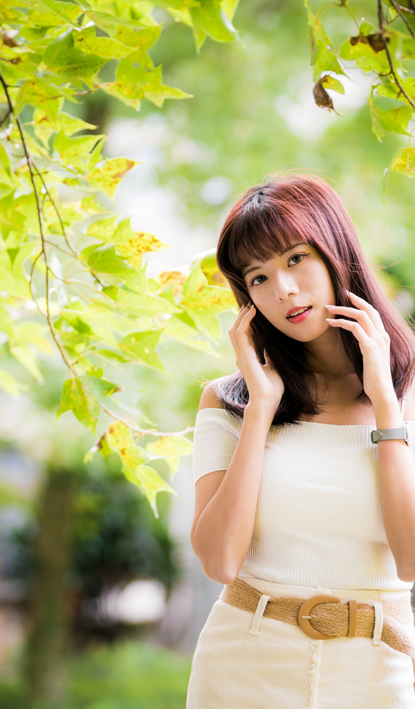 Красивая азиатка в белом платье у дерева 