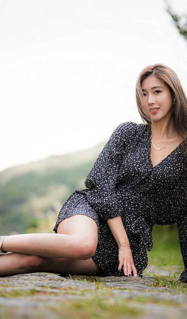 Красивая девушка азиатка в платье лежит на земле 