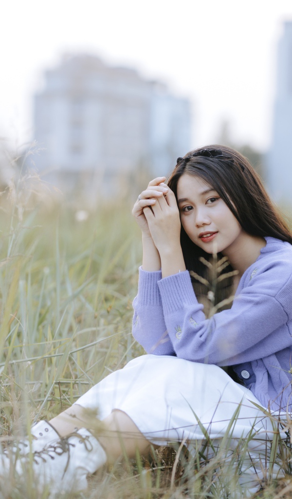 Красивая девушка азиатка сидит на поле с травой 