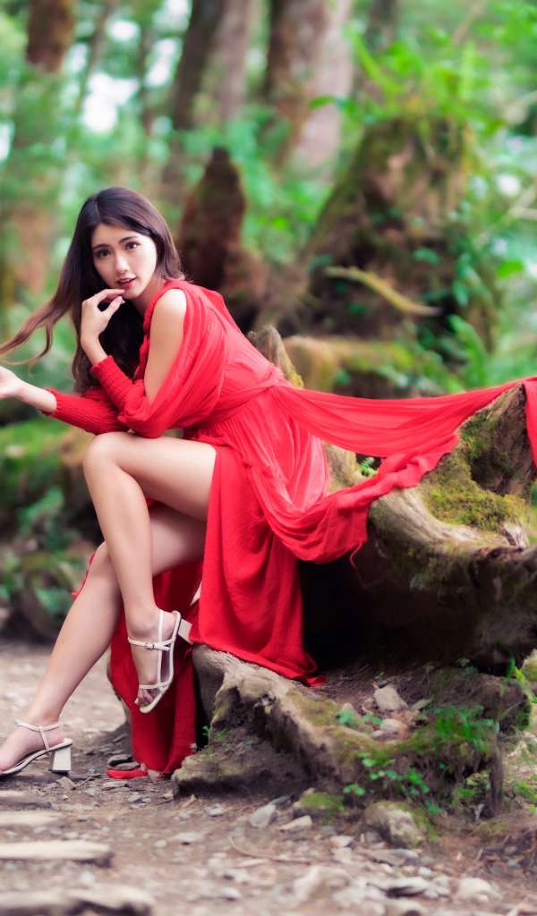 Красивая азиатка в красном платье сидит на дереве 