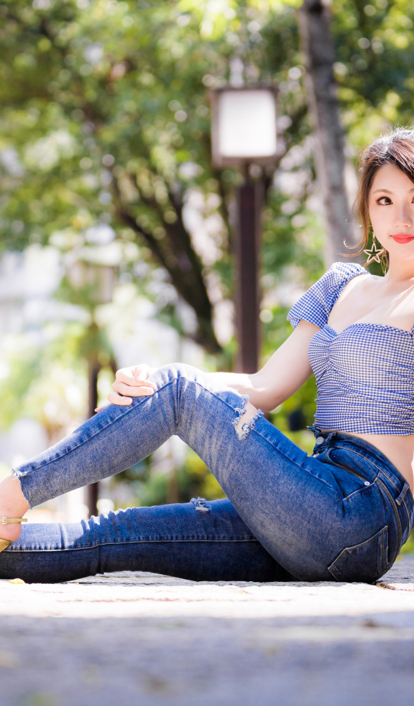 Красивая азиатка в джинсах сидит на земле