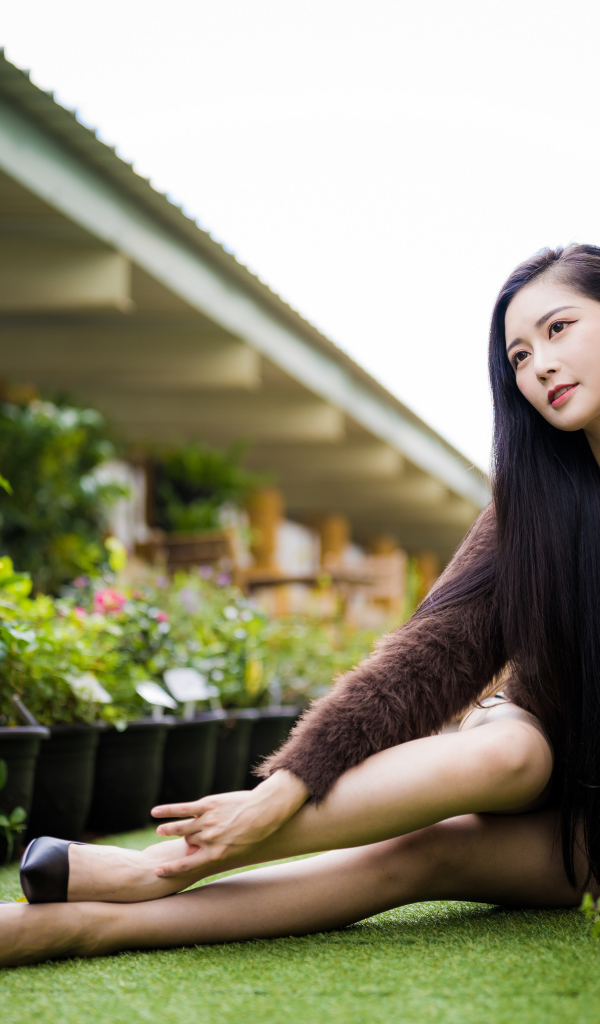 Красивая азиатка сидит на земле у цветов