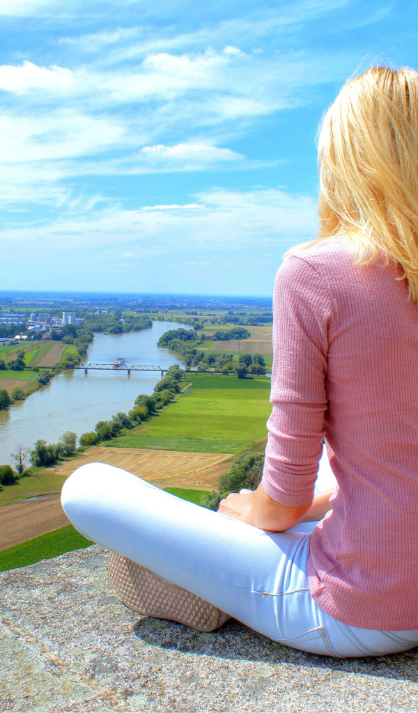 Красивая блондинка сидит на камне у реки