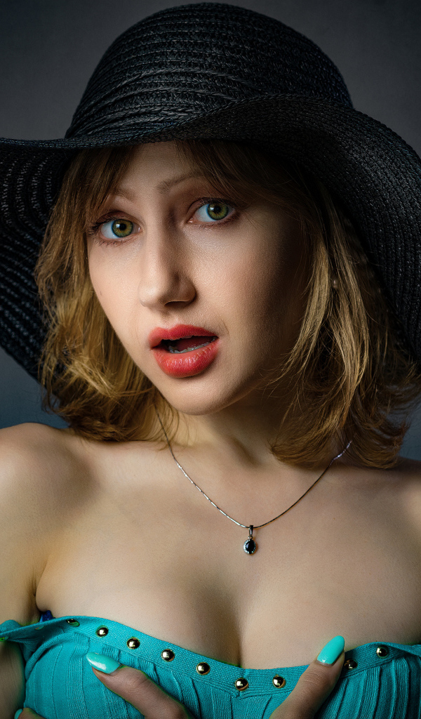 Красивая девушка в большой черной шляпе на сером фоне 