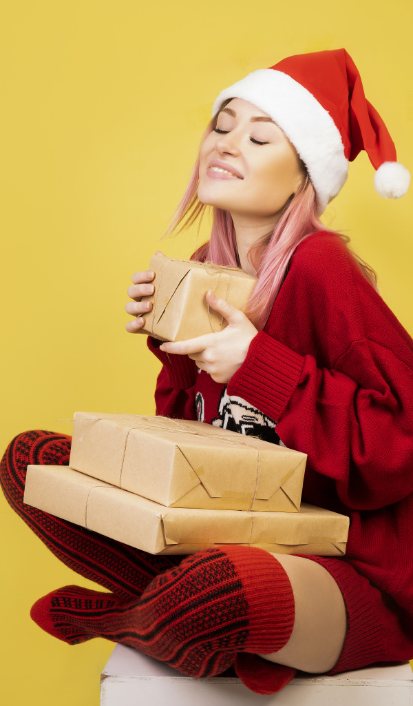 Красивая девушка в новогоднем костюме с подарками на желтом фоне