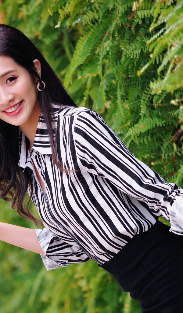 Красивая девушка в полосатой рубашке стоит у растения