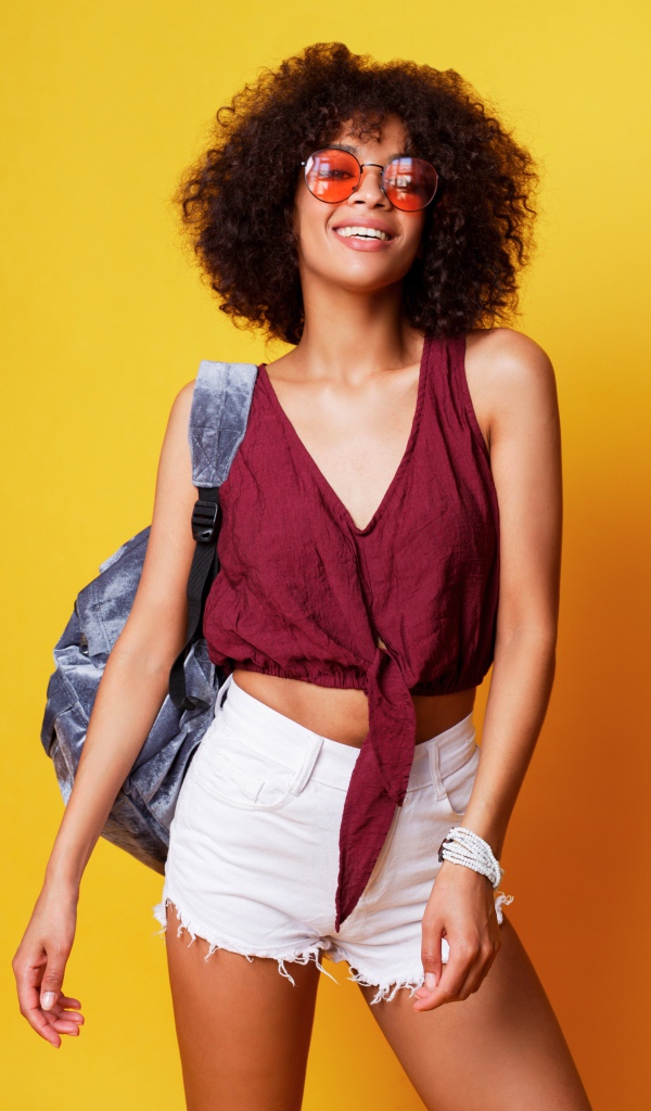 Красивая девушка в очках с рюкзаком на желтом фоне 