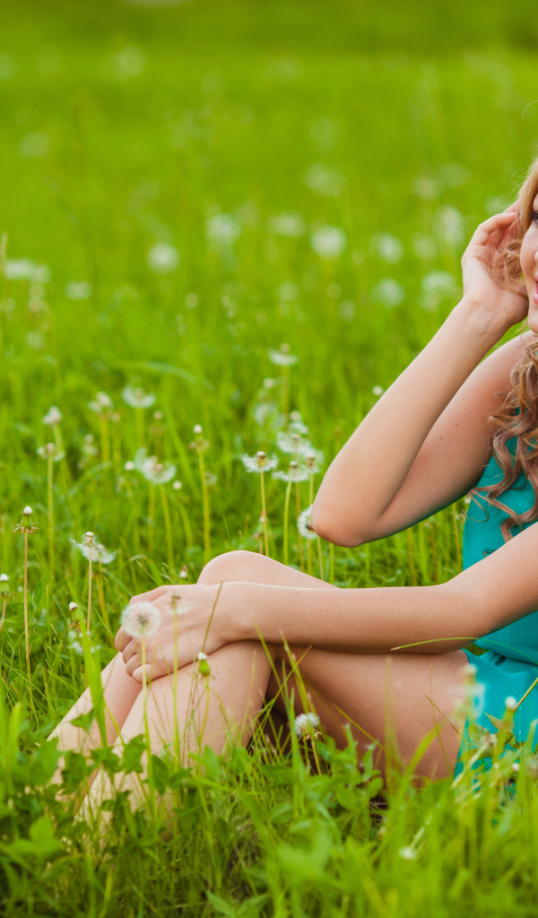 Красивая девушка с наушниками на голове  сидит на траве