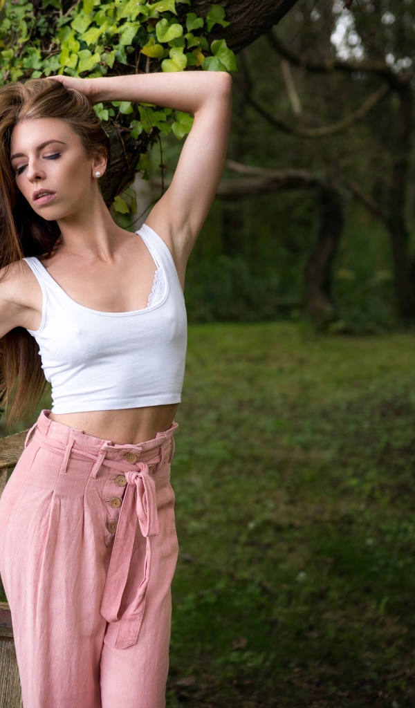 Красивая стройная девушка стоит у дерева 