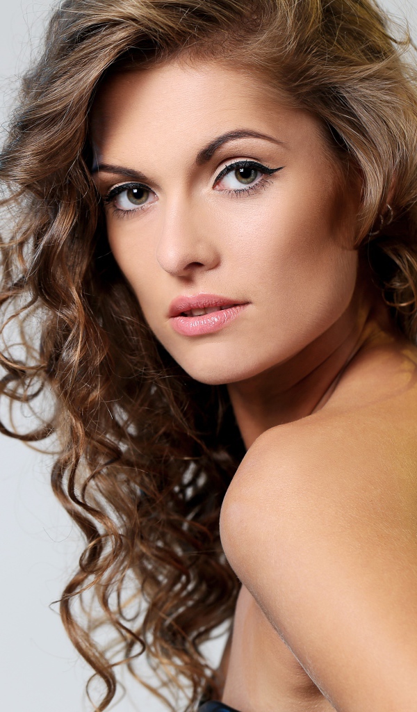 Вьющиеся волосы у красивой девушки на сером фоне