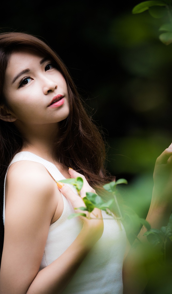 Милая азиатка в белом стоит у зеленых листьев