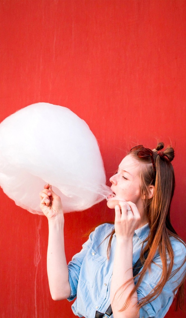 Девушка ест сладкую вату на красном фоне 