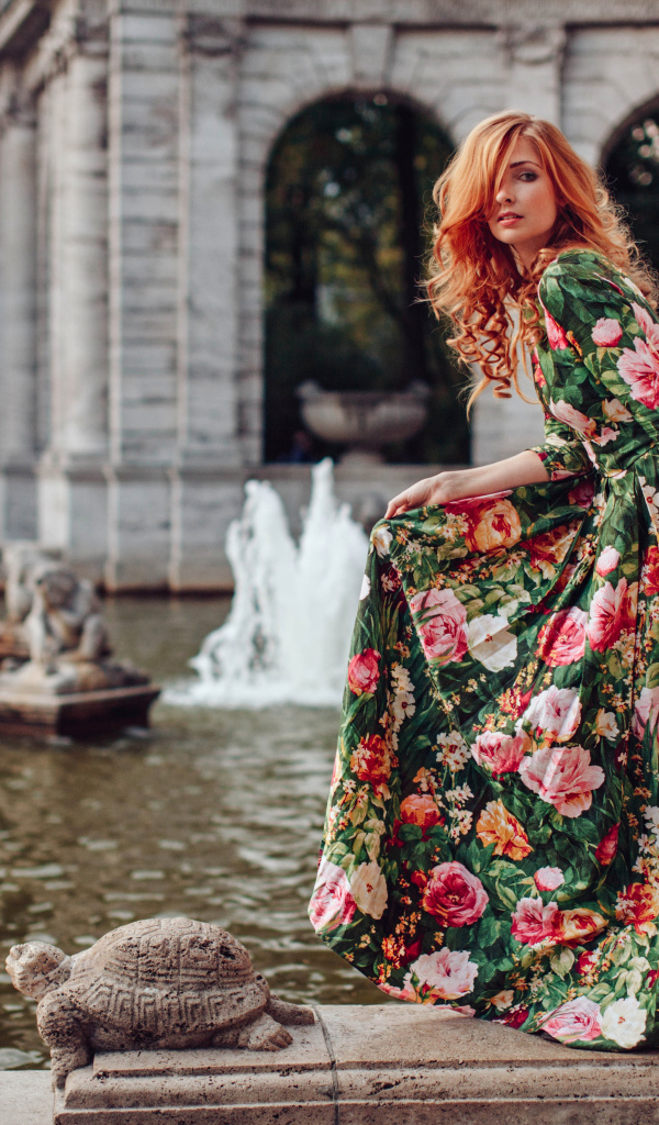 Девушка в красивом цветастом платье у пруда в парке 