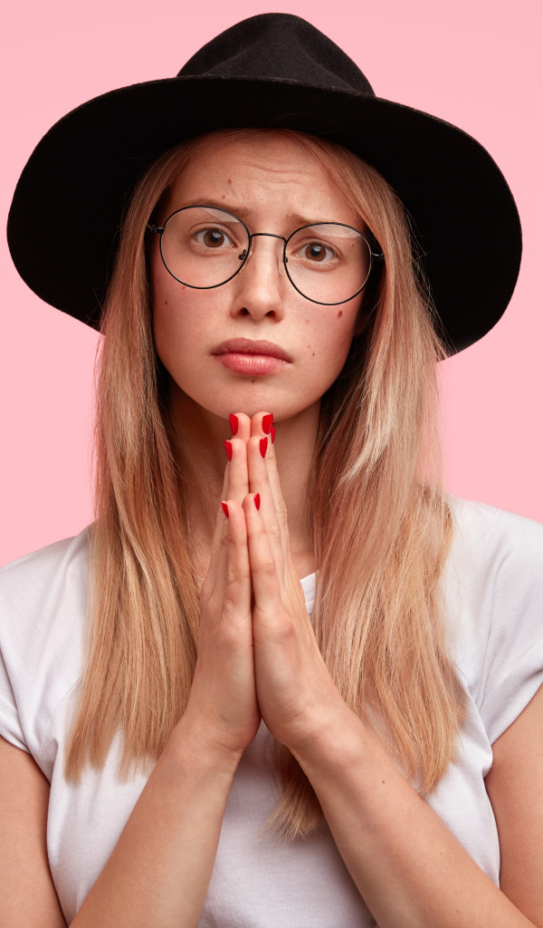 Girl in a black hat on a pink background asks for forgiveness