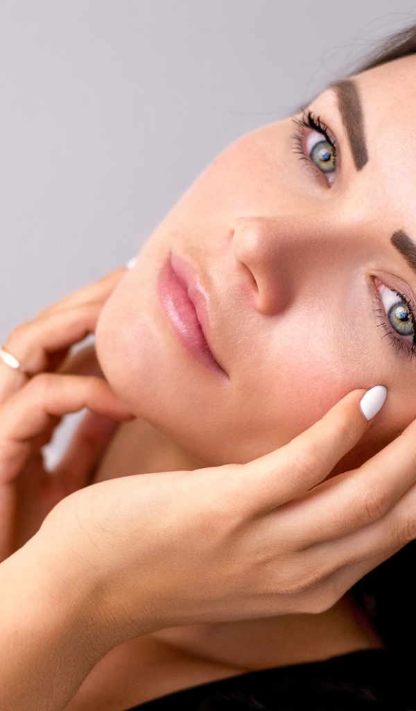 Девушка с руками у лица на сером фоне