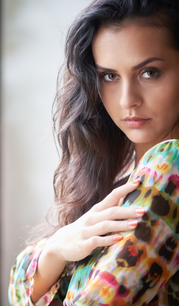 Длинноволосая кареглазая девушка стоит у окна