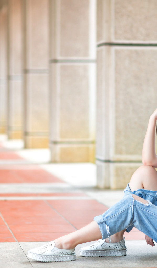 Грустная девушка азиатка сидит у колонны