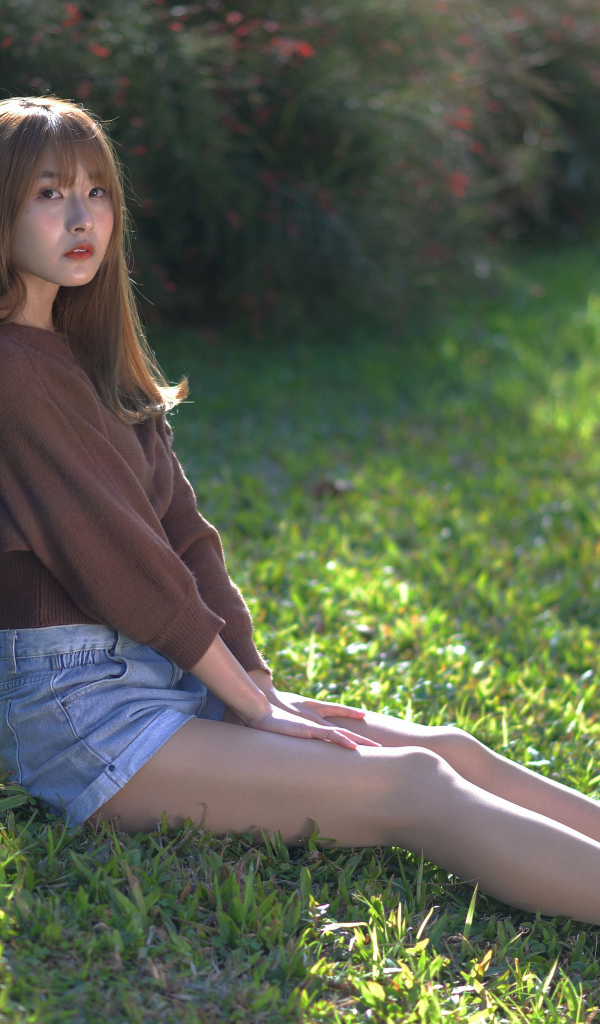 Грустная девушка азиатка сидит на зеленой траве 