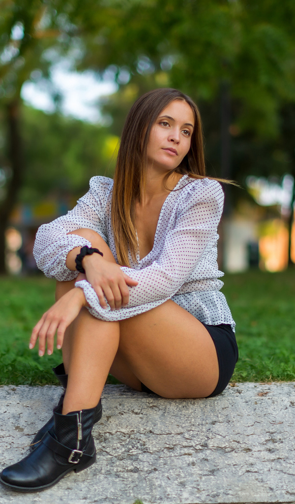 Грустная девушка сидит на земле в парке 