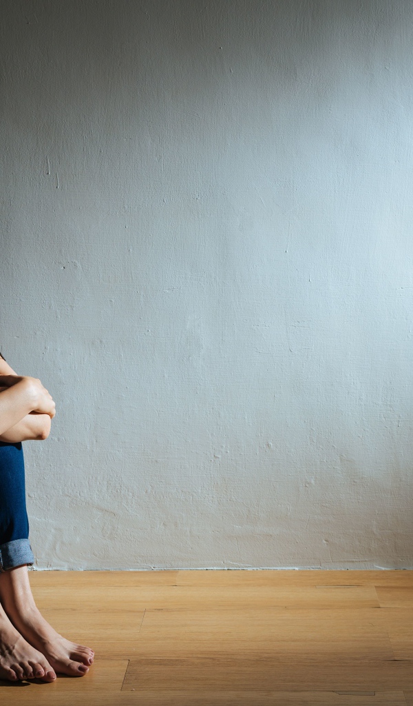 Испуганная девушка азиатка сидит у стены