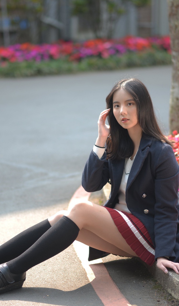 Девушка школьница сидит на земле у клумбы 