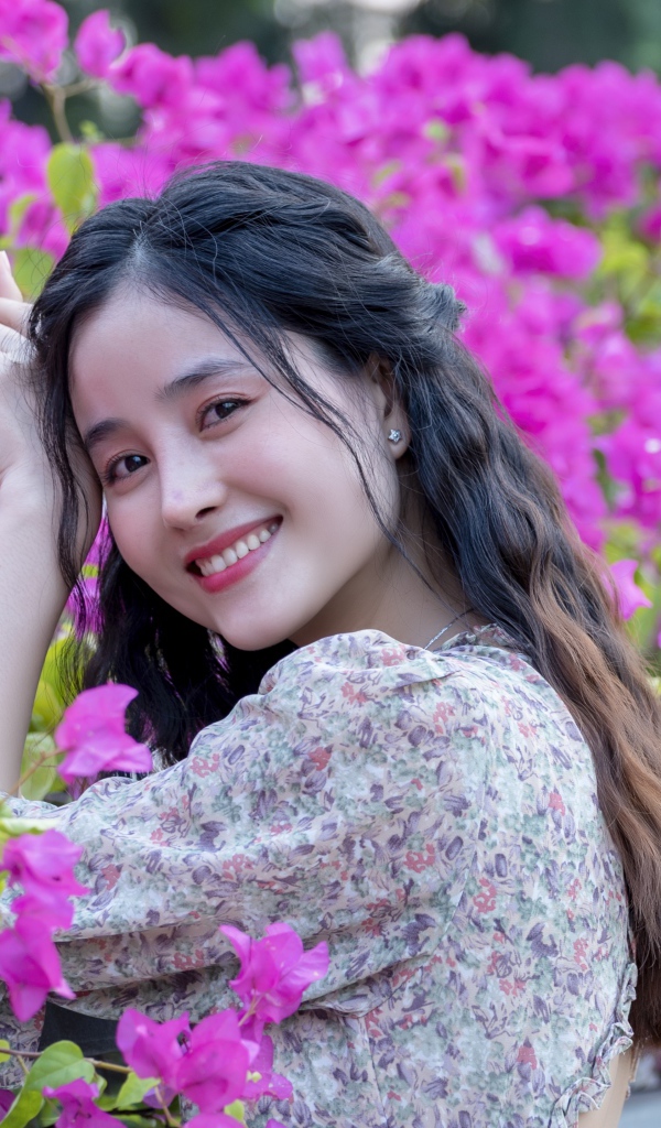 Улыбающаяся девушка азиатка на фоне розовых цветов