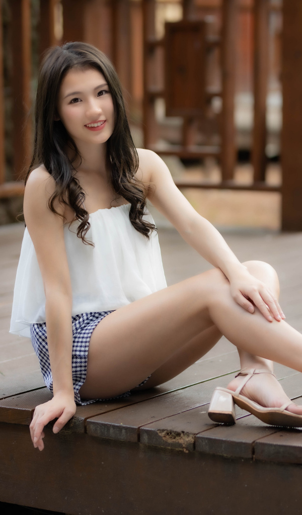 Улыбающаяся девушка азиатка сидит на мосту 