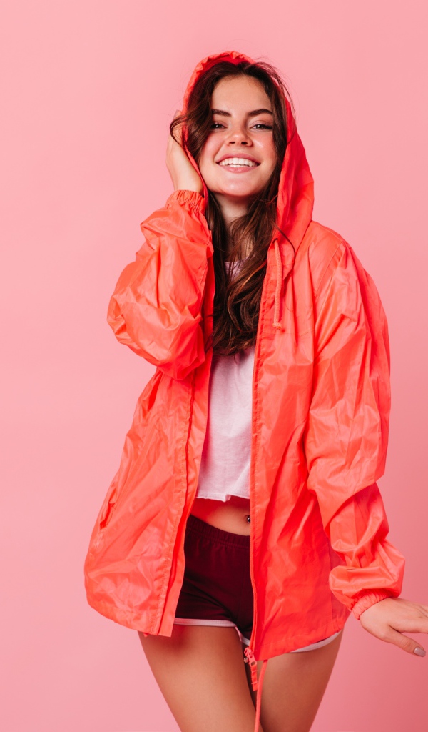 Улыбающаяся девушка в плаще на розовом фоне