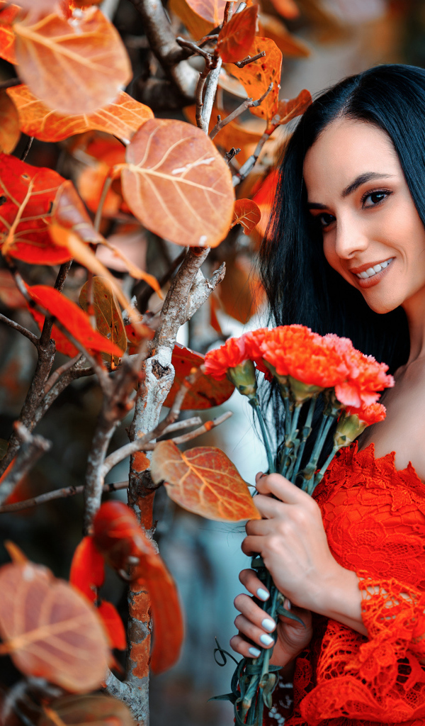 Улыбающаяся девушка с букетом гвоздик у стены с осенними листьями