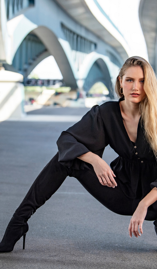 Стильная девушка в черном костюме под мостом