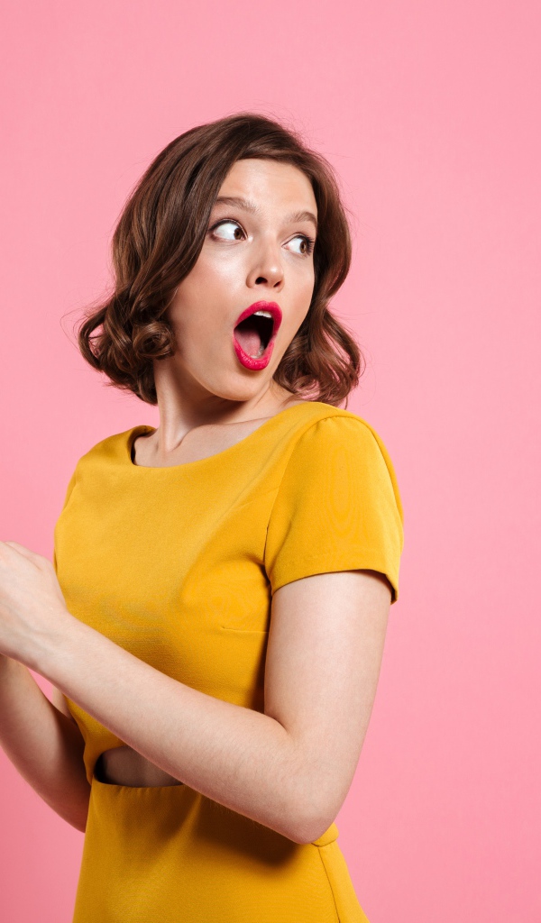 Удивленная девушка с телефоном в руках на розовом фоне