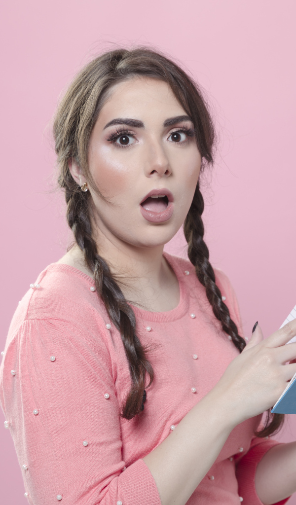 Удивленная девушка с книгой на розовом фоне