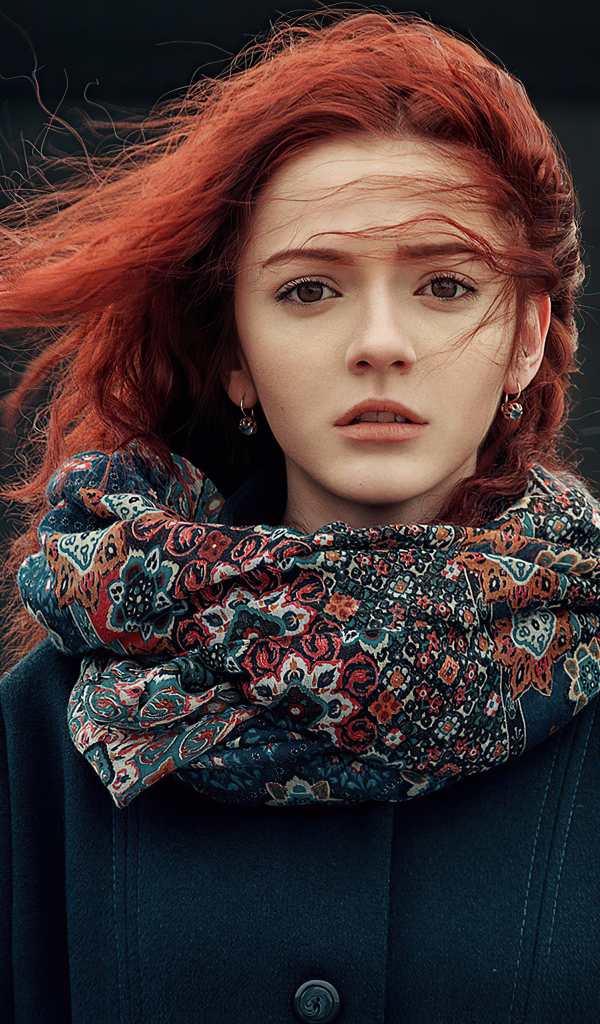 Ветер развивает волосы рыжеволосой девушки в пальто