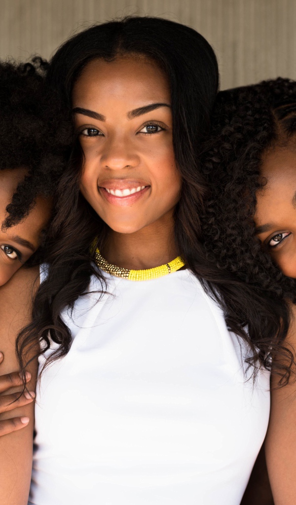 Три улыбающиеся темнокожие девушки на фоне стены 