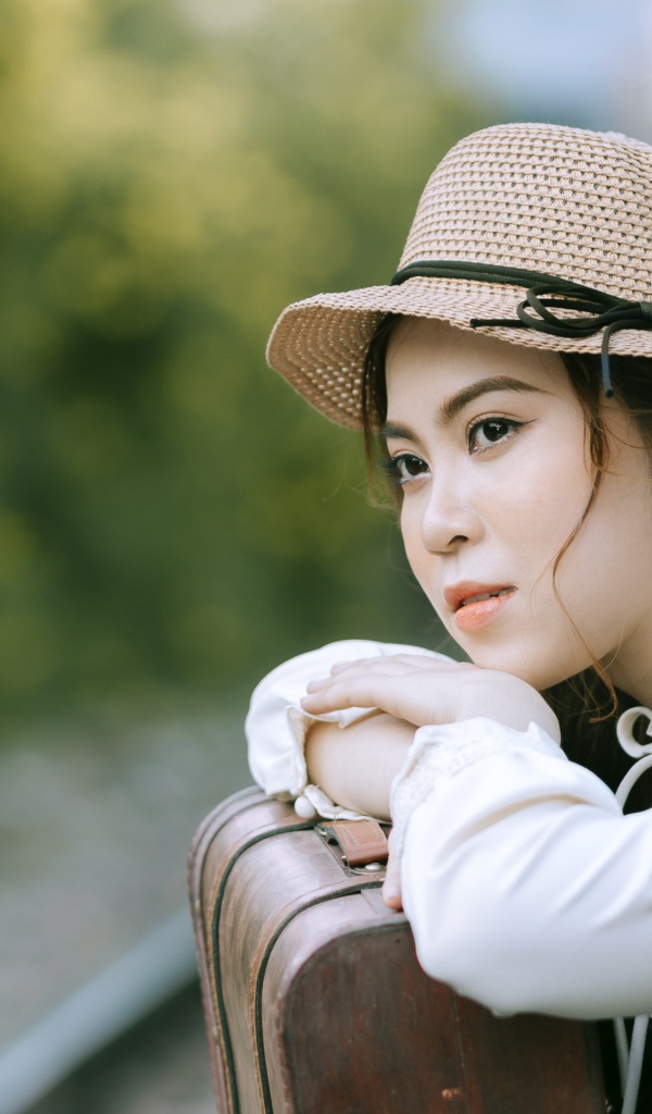 Молодая азиатка в шляпе с чемоданом