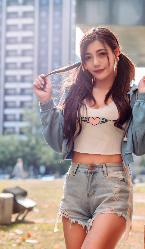 Молодая азиатка в коротких шортах стоит у стены