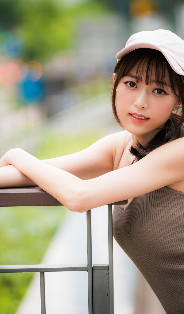 Молодая азиатка в кепке у перил 