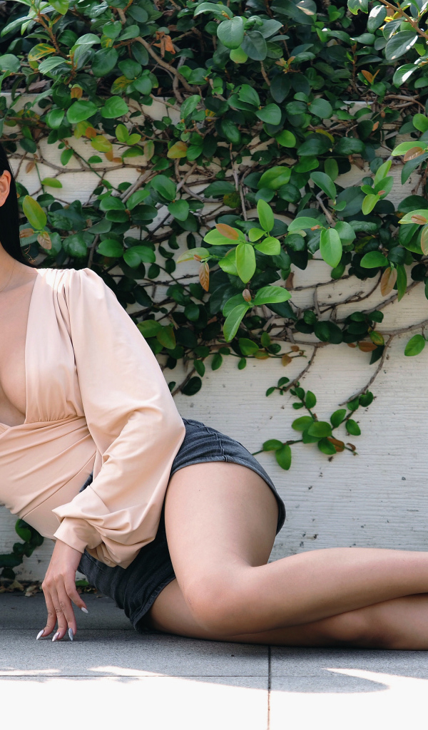 Молодая девушка азиатка с длинными волосами лежит на земле у стены 