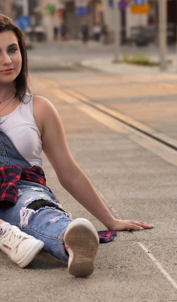 Молодая девушка в джинсовом наряде сидит на асфальте